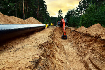 Excavator dig trench at forest area sunset background. Backgoe on earthwork for laying crude oil...