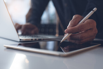 Business man using stylus pen on digital tablet and working on laptop in modern office