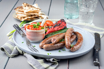 Modern style traditional barbecue Bratwurst with vegetable, relish and yufka bread served as close-up on a Nordic design plate