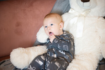 thoughtful newborn baby and big white teddy bear sitting on sofa or couch,fingers in mouth