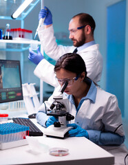 Scientist looking at blood sample through microscop and assitant taking liquid with micropipette....