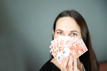 finance, investment and saving concept - young woman covering her face with fan of euro money over grey background