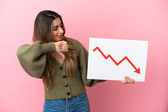 Young caucasian woman isolated on pink background holding a sign with a decreasing statistics arrow symbol and doing bad signal