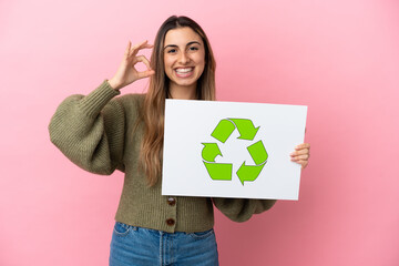 Young caucasian woman isolated on pink background holding a placard with recycle icon and celebrating a victory