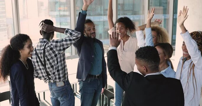 Seven diverse employees putting hands together in center of circle, then raise and cheering, make one for all gesture of unity and teamwork, synergy and loyalty. Team building meeting activity concept
