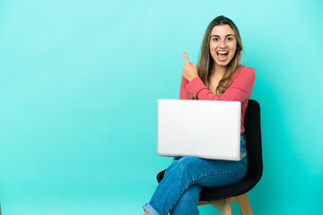 Young caucasian woman sitting on a chair with her pc isolated on blue background surprised and pointing side