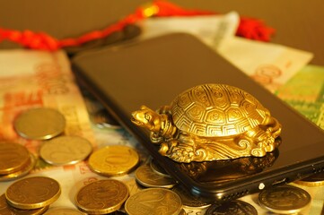 A metal turtle with coins and a phone on the table. Business concept.