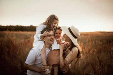 Stylish charming Caucasian young family with two children hugging in summer at sunset, girl kid blond with Down syndrome with parents and younger sister, brown chocolate tinting, family values