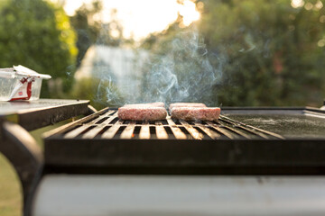Burgers cooking over flames on grill - leisure, food and holidays concept