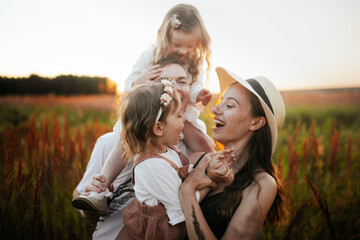 Stylish charming Caucasian young family with two children hugging in summer at sunset, girl kid...