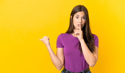 Fototapeta premium Teenager Brazilian girl over isolated yellow background pointing to the side and doing silence gesture