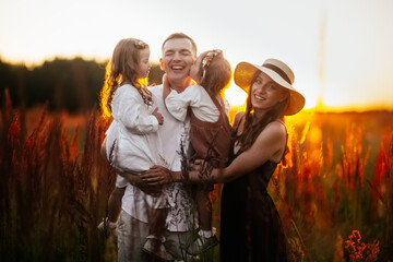 Stylish charming Caucasian young family with two children hugging in summer at sunset, girl kid blond with Down syndrome with parents and younger sister, brown chocolate tinting, family values