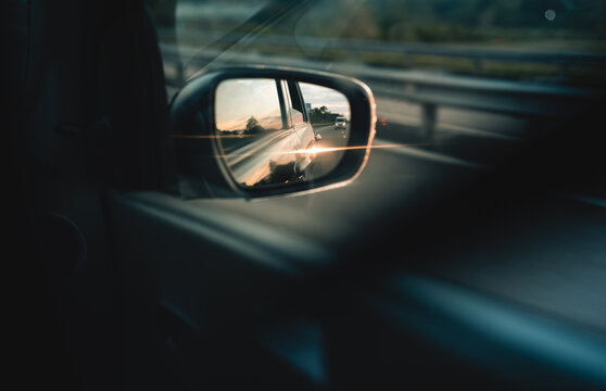 Car side mirror and the reflecting evening sunlight from the car body and glowing in the highway. fast-moving automobile concept. side mirror view from the rear passenger sheet. © nilanka