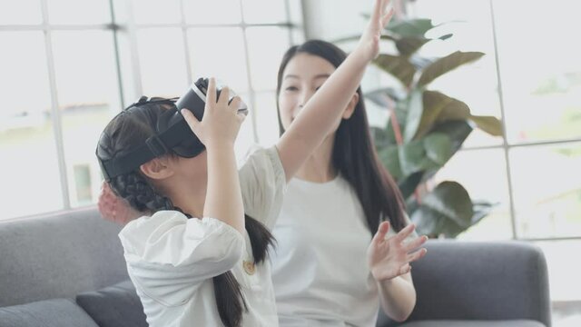 Young Asian kid girl wearing virtual reality, VR gamer VDO and play with mom on living room, relax and fun with high technology at home concept