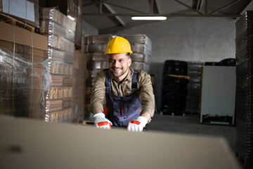 Portrait of caucasian smiling warehouse worker pushing load and palettes on manual forklift in storage room.