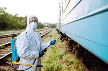 Man in Hazmat suit, protective gloves and goggles use sprayer equipment disinfect a train. Covid-2019.