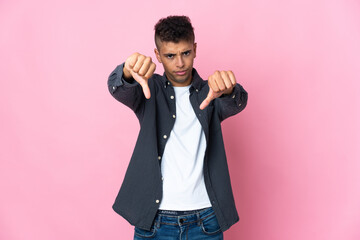 Young Brazilian man isolated on pink background showing thumb down with two hands