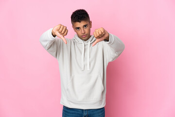 Young Brazilian man isolated on pink background showing thumb down with two hands