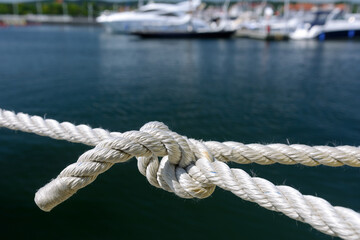 Fototapeta premium Yachting and marine concept. Close-up of a sea knot on a blurred background of boats moored in the harbor