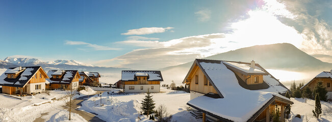 Snowy housing estate in the mountains with houses. In the background the Alps and a cloudy sky. Copy space