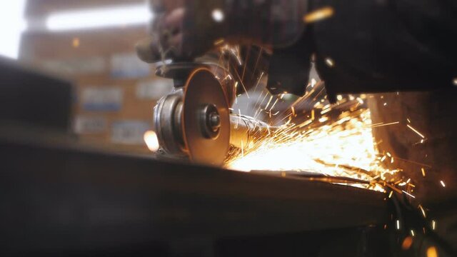 A man with a grinder saws off a metal billet in the workshop. Close-up of sparks flying around in slow motion.