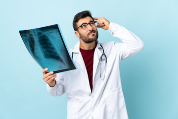 Professional traumatologist holding radiography isolated on blue background having doubts and with confuse face expression