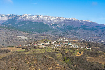 Fototapeta na wymiar Panoramic view of the snow-capped mountains and the mountain village at their foot in early spring