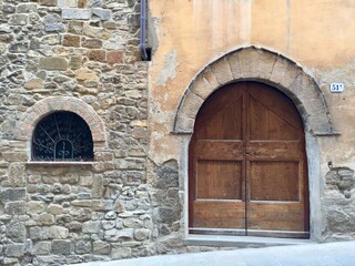 Fototapeta na wymiar Italian medieval house with wooden door and arch. Fragment of facade with stone wall, medieval building. Photo made in Toscana. Date of photo is 28.09.2015