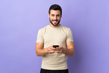 Young handsome man with beard over isolated background sending a message with the mobile