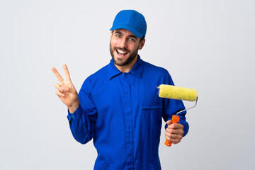 Painter man holding a paint roller isolated on white background smiling and showing victory sign