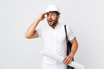 Young architect man with helmet and holding blueprints isolated on white background with surprise expression while looking side