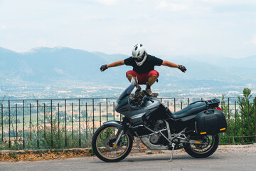 Obraz premium A lightly dressed man and his adventure motorcycle. No protection, only helmet. Sunny day in Narni, Italy. Green mountains in the background. Vacation and travel concept
