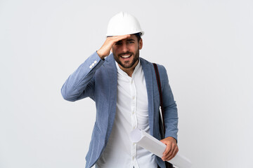 Young architect man with helmet and holding blueprints isolated on white background looking far away with hand to look something