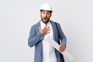 Young architect man with helmet and holding blueprints isolated on white background surprised and...