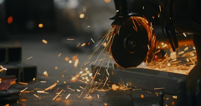 Worker cuts a metal profile with a grinder in slow motion with a flying stream of sparks, metalwork in blacksmith's workshop, 4k 60p Prores HQ