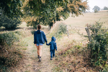 Maman se balade avec son enfant, main dans la main, de dos, en été sous la pluie