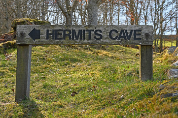 Wooden sign for Hermits Cave with arrow, blurred rural background. Taken in Perthshire, Scotland near Falls of Acharn