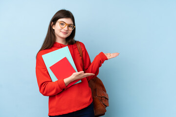 Young Ukrainian teenager student girl holding a salad over isolated blue background extending hands to the side for inviting to come