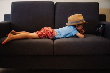 petit garçon couché sur le ventre dans un divan, en été, en vacances avec un chapeau sur la...
