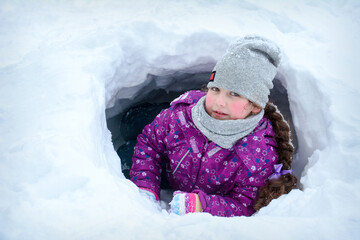 Fototapeta na wymiar Girl Laying In Snow Tunnel On Winter Day