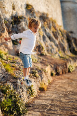 Naklejka na ściany i meble Jeune garçon, en chemise blanche, joue dans les rochers, en vacances, en été, grimpe, saute, escalade