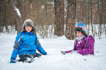 Fototapeta na wymiar In winter, in a snowy pine forest, a brother and sister sit in a snowdrift.