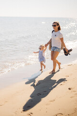 Maman et sa petite fille se promènent les pieds dans l'eau à la plage, en vacances, en été, en se tenant par la main. 