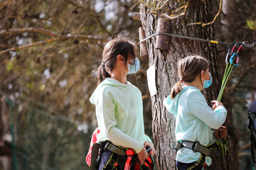 Fototapeta na wymiar girls with sportswear and coronavirus protection mask, jumping from tree to tree, canopy installation, forest in the background