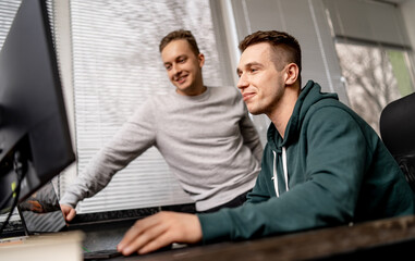 Handsome programmer working in casual cloth at computer. Young guy discussing new project.