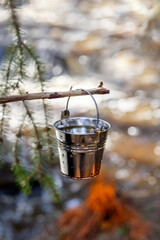 Aluminum bucket with waterhung on a wooden stick hanging over the fire. Water protection concept. Close-up. Place for your text. High quality photo