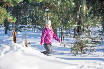 In winter, on a bright sunny day in a snowy forest, a girl plays near a snowdrift.