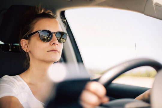 Jeune femme conduit une voiture, en été, avec des lunettes de soleil