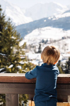 Petit enfant regarde la vue de son balcon sur la montagne en hiver au ski