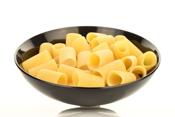 Bright yellow uncooked pasta in a black ceramic plate, close-up, isolated on white.